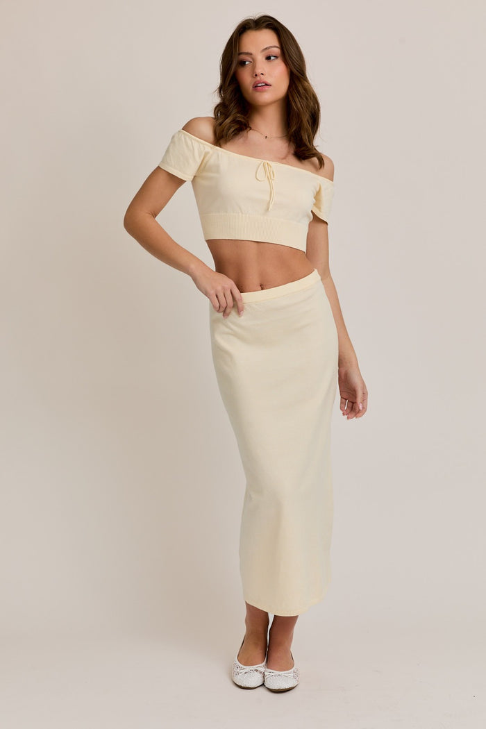 woman wearing a cream off-the-shoulder crop top and a matching long skirt, styled with white shoes