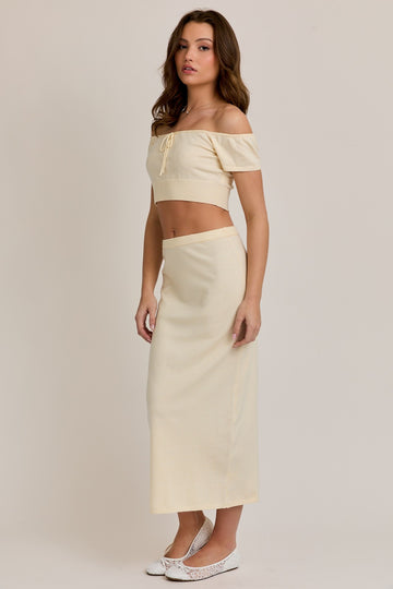 woman wearing a cream cropped off-shoulder top and a matching long skirt, styled with white ballet flats