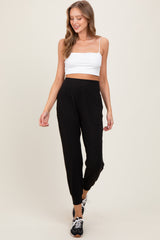 woman wearing a white cropped tank top and black jogger pants with pockets, smiling and walking against a neutral background