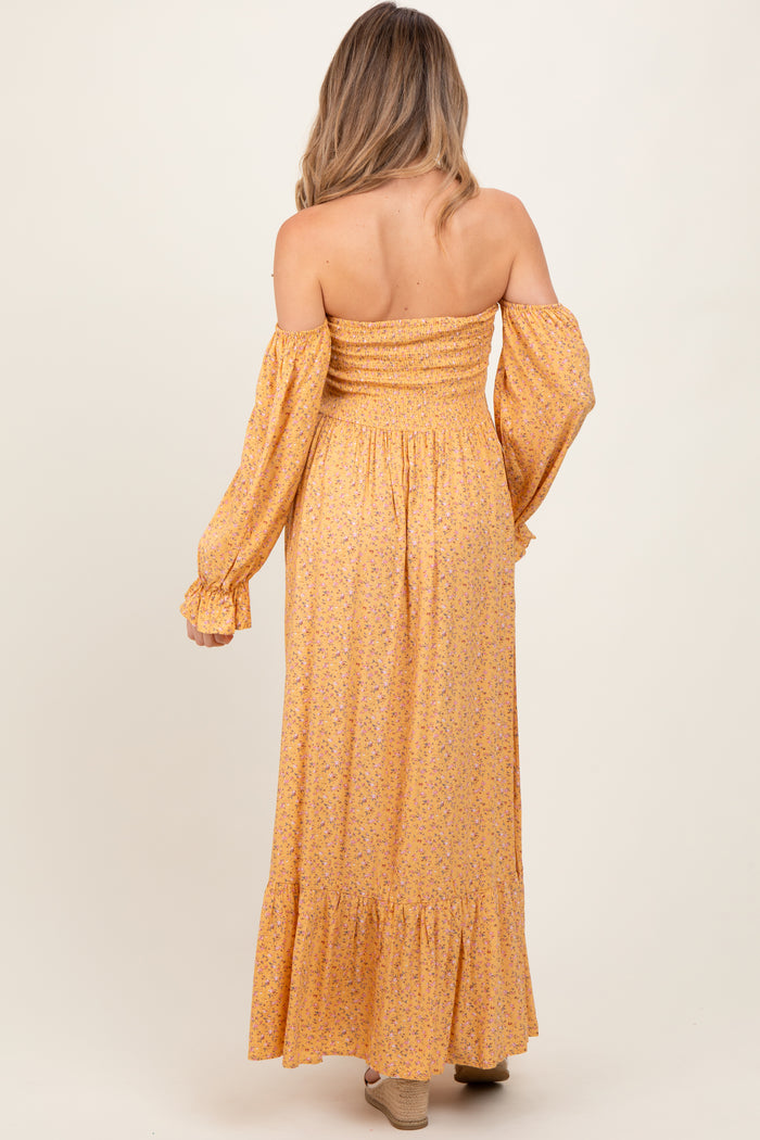 woman wearing a yellow floral off-the-shoulder maternity dress with long sleeves and a ruffled hem