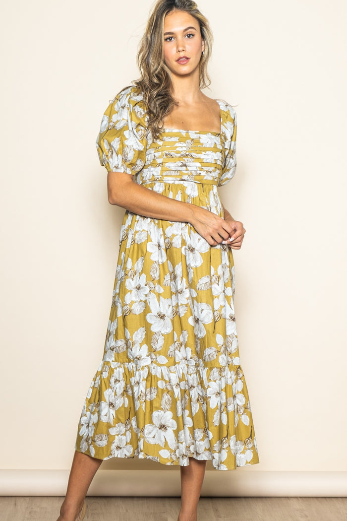 woman wearing a yellow floral midi dress with puff sleeves and a square neckline, standing against a light background