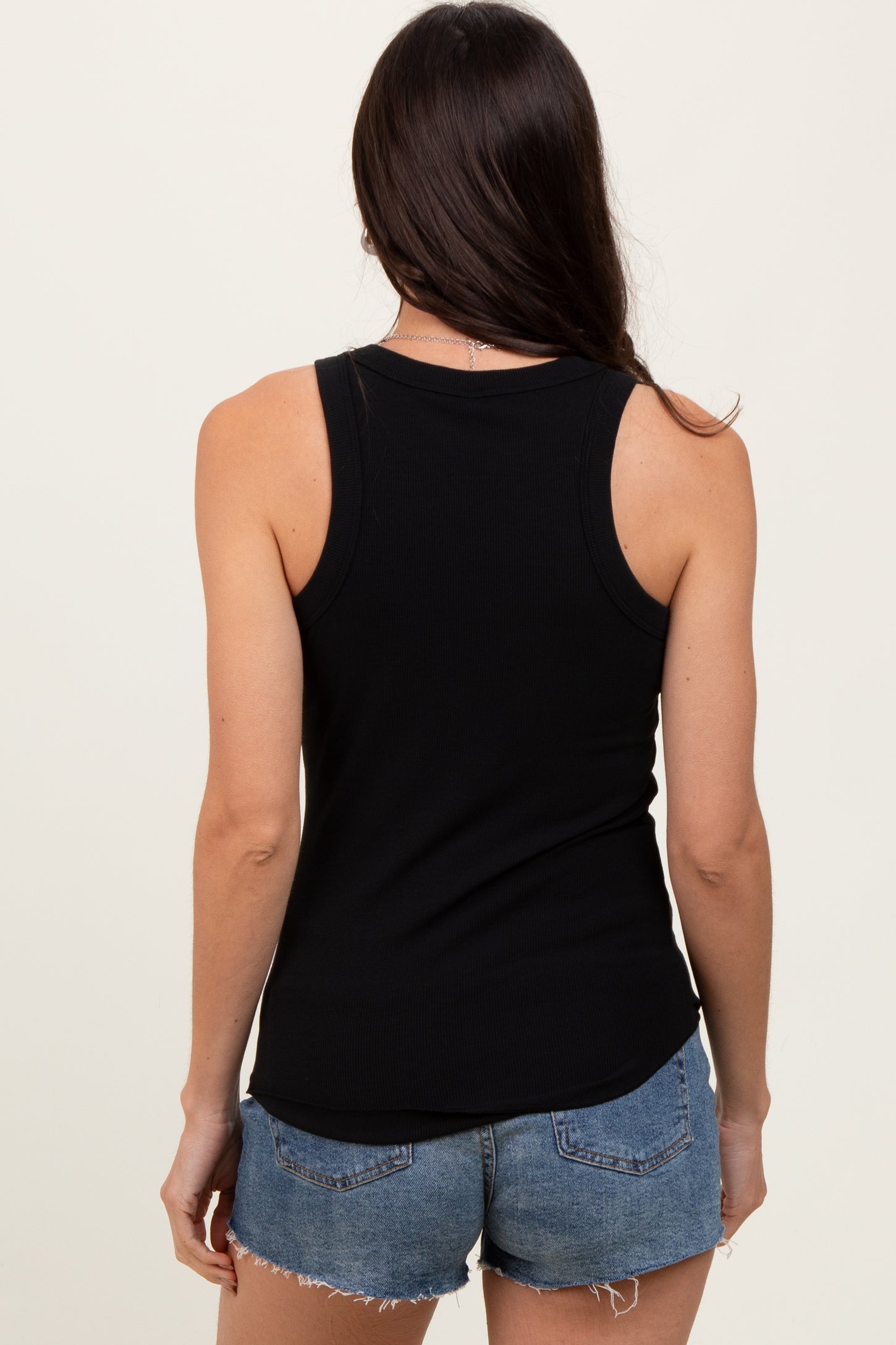 woman wearing a black ribbed tank top and denim shorts, seen from the back