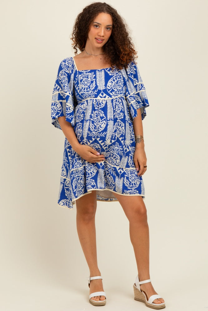 woman wearing a blue floral maternity dress with short sleeves and a baby bump on display