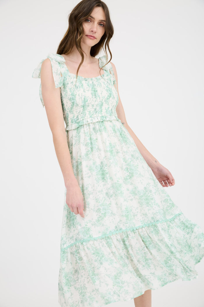 woman wearing a floral print midi dress in green and white with ruffled straps and a tiered skirt