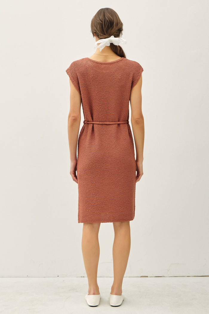 woman wearing a rust-colored knitted dress with a belted waist and short sleeves, viewed from the back