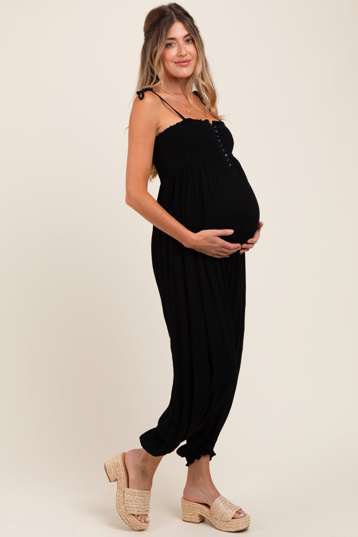 woman wearing a black maternity jumpsuit with buttons and holding her baby bump