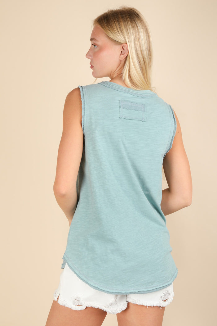 woman wearing a light blue sleeveless top with a rounded hem and patch detail, styled with white distressed shorts