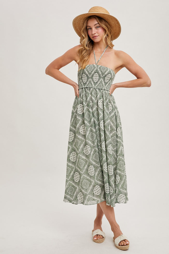 woman wearing a green patterned strapless midi dress and a straw hat, standing with hands on hips