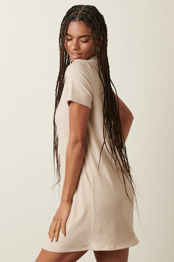 woman wearing a beige short sleeve ribbed dress, showing a relaxed fit and a playful pose from behind