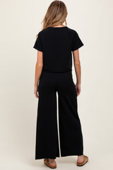 woman wearing a black short sleeve maternity jumpsuit with wide leg pants, showing the back view