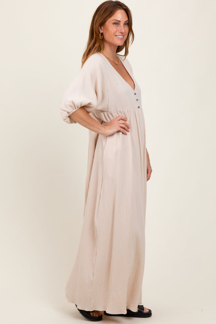 woman wearing a beige maxi dress with a deep v-neck and button detail, featuring loose sleeves and a flowy silhouette
