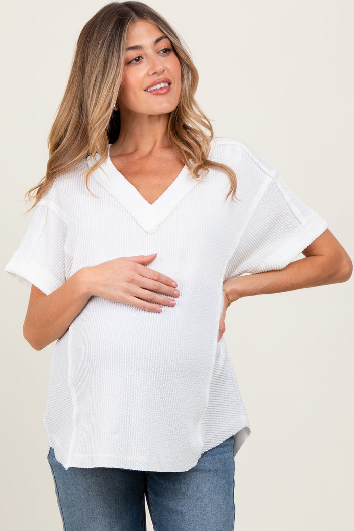 woman wearing a white short sleeve v-neck maternity top and gently holding her baby bump