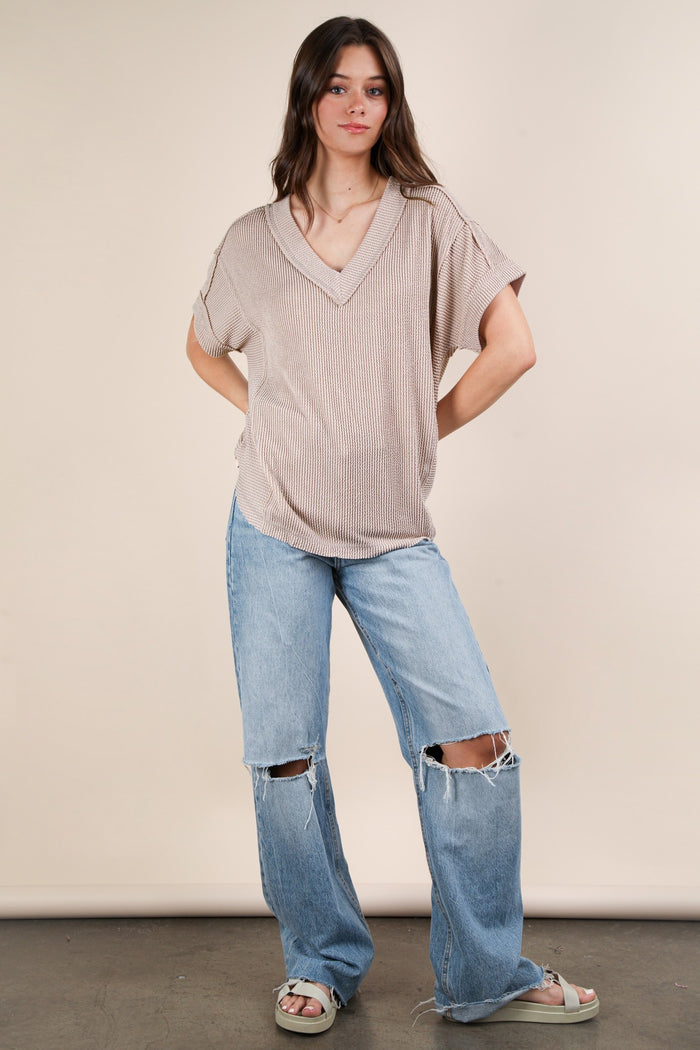 woman wearing a ribbed beige v-neck top and distressed oversized light blue jeans