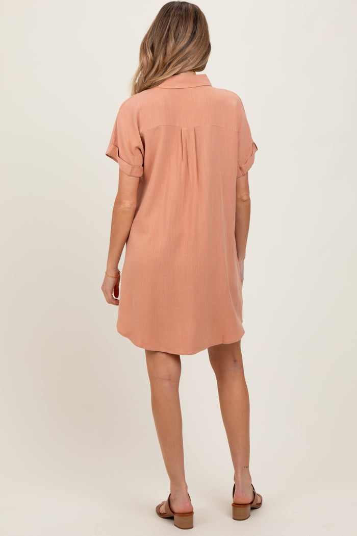 woman wearing a blush pink short sleeve maternity dress with a relaxed fit and back pleat detail.