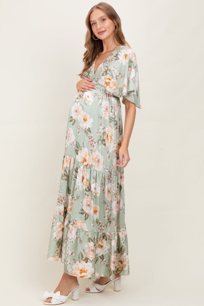 woman wearing a floral mint green maternity maxi dress with short sleeves and a v-neck, cradling her baby bump