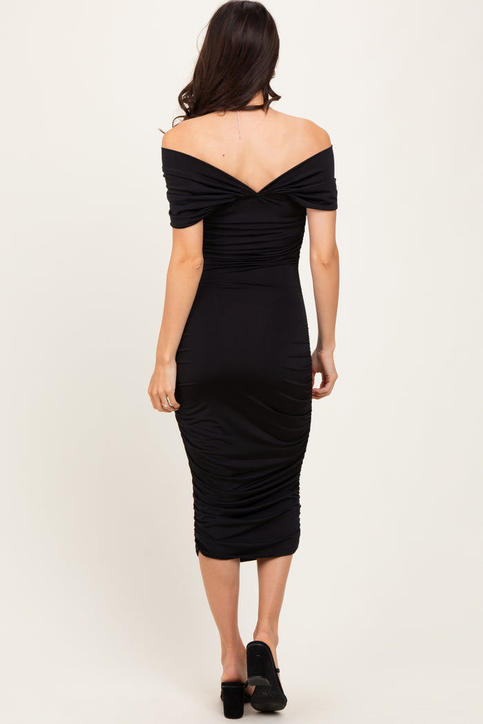 woman wearing a black off-the-shoulder ruched midi dress, showing the back view and fitted silhouette