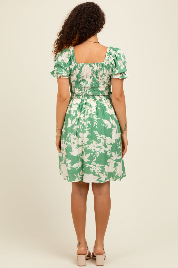 woman wearing a green floral maternity dress with puff sleeves and a smocked back, showcasing her baby bump