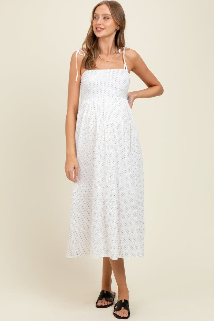 woman wearing a white polka dot maternity dress with spaghetti straps and a flowy skirt, showcasing her baby bump