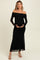 woman wearing a black off-the-shoulder maternity dress with long sheer sleeves and holding her baby bump