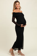 woman wearing a black off-the-shoulder maternity dress with long sheer sleeves and a visible baby bump