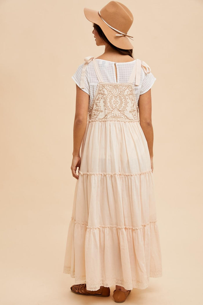 woman wearing a light beige tiered maxi dress with a lace-back detail and a tan wide-brim hat