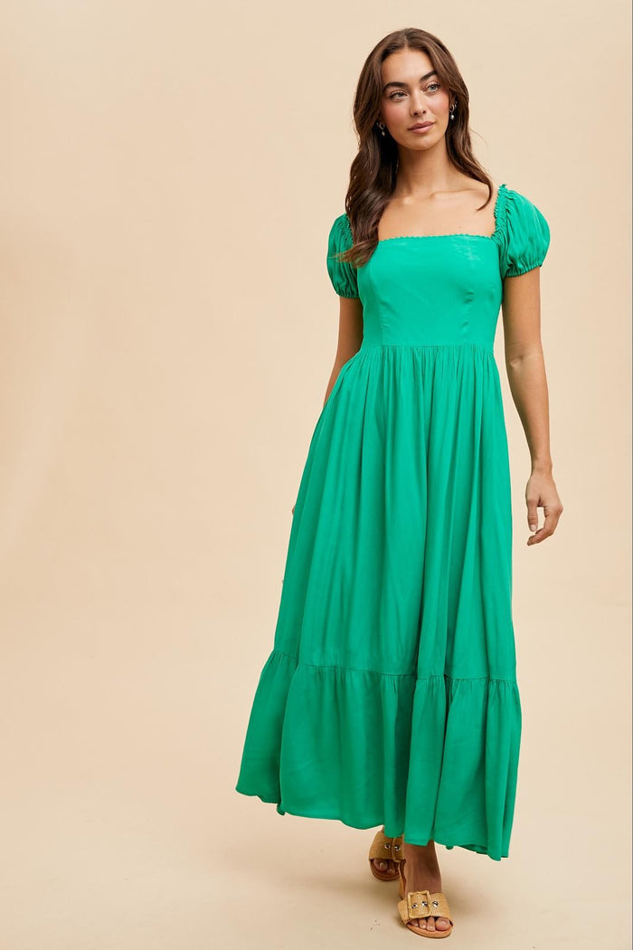 woman wearing a bright green maxi dress with puff sleeves and a square neckline, styled with golden sandals