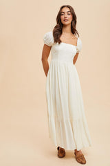 woman wearing a white puff sleeve maxi dress with a square neckline and tiered hem, posed against a neutral background