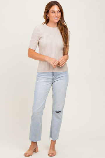 woman wearing a light beige ribbed short sleeve top and light wash distressed jeans, standing and smiling