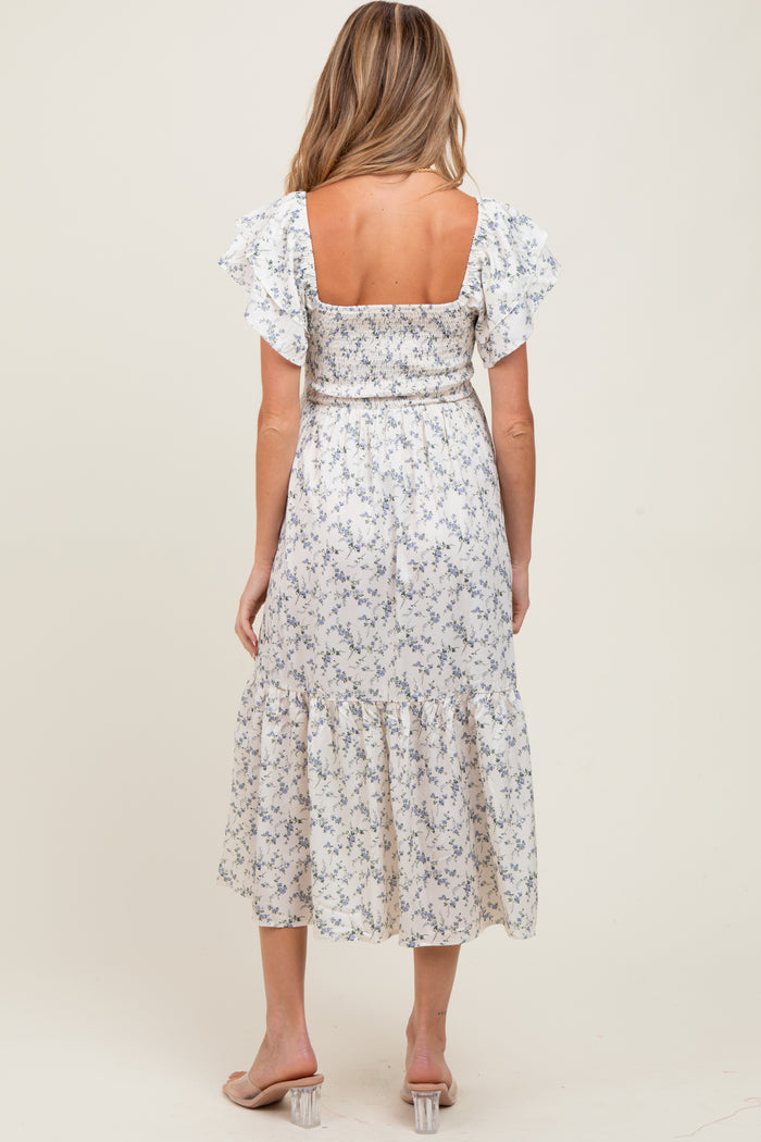 woman wearing a floral print maternity dress with short ruffle sleeves and a belted waist, showing her baby bump