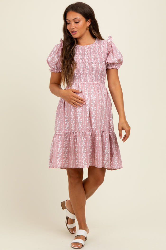 woman wearing a pink floral print smocked maternity dress with puff sleeves and a tiered skirt, holding her baby bump