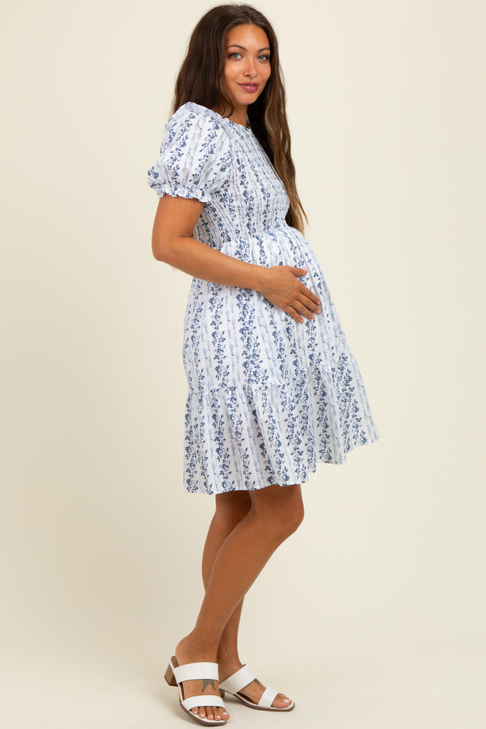 woman wearing a white floral puff sleeve maternity dress and holding her baby bump