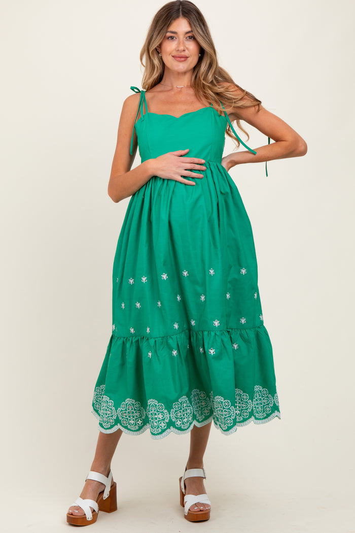 woman wearing a green maternity dress with embroidered details and a flowing silhouette, holding her baby bump
