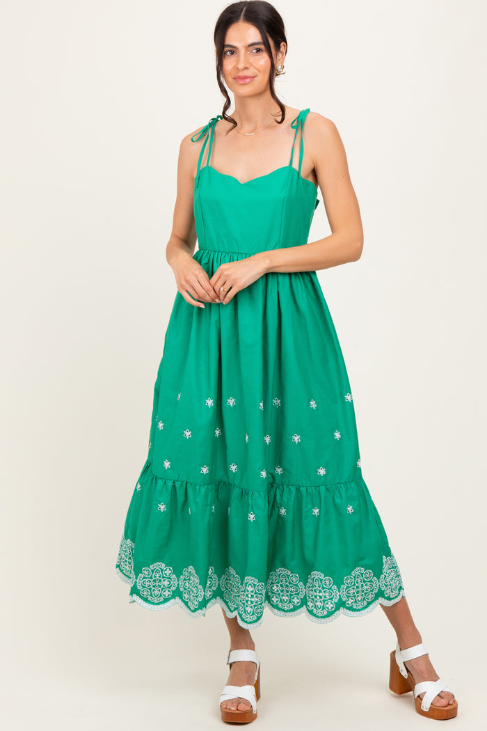 woman wearing a green sleeveless maxi dress with adjustable straps and embroidery details at the hem