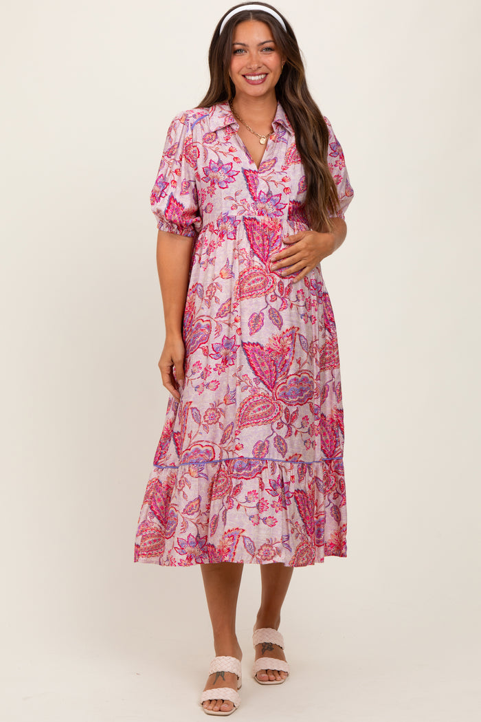 woman wearing a pink floral maternity dress with short puff sleeves and a tiered skirt, holding her baby bump