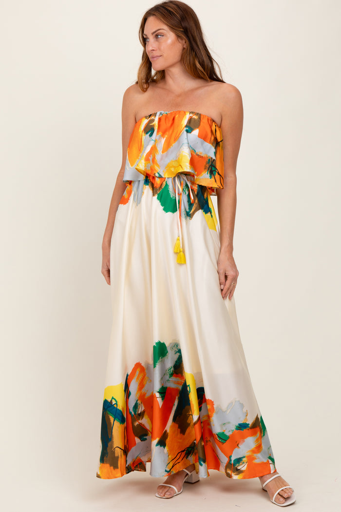 woman wearing a strapless floral maxi dress in orange, green, and yellow with a ruffled top and tie detail at the waist
