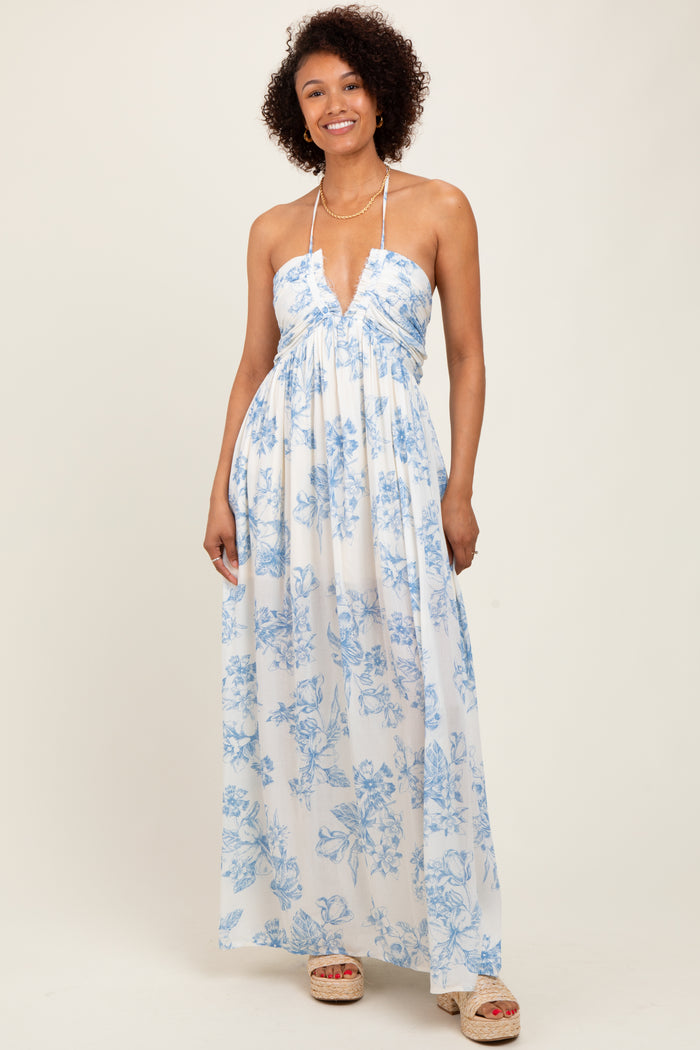 woman wearing a white floral maxi dress with blue print and halter neckline, smiling at the camera