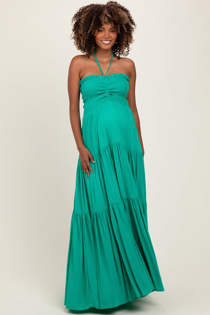 woman wearing a green strapless maternity maxi dress with a halter neck and a flowing tiered skirt, showcasing her baby bump