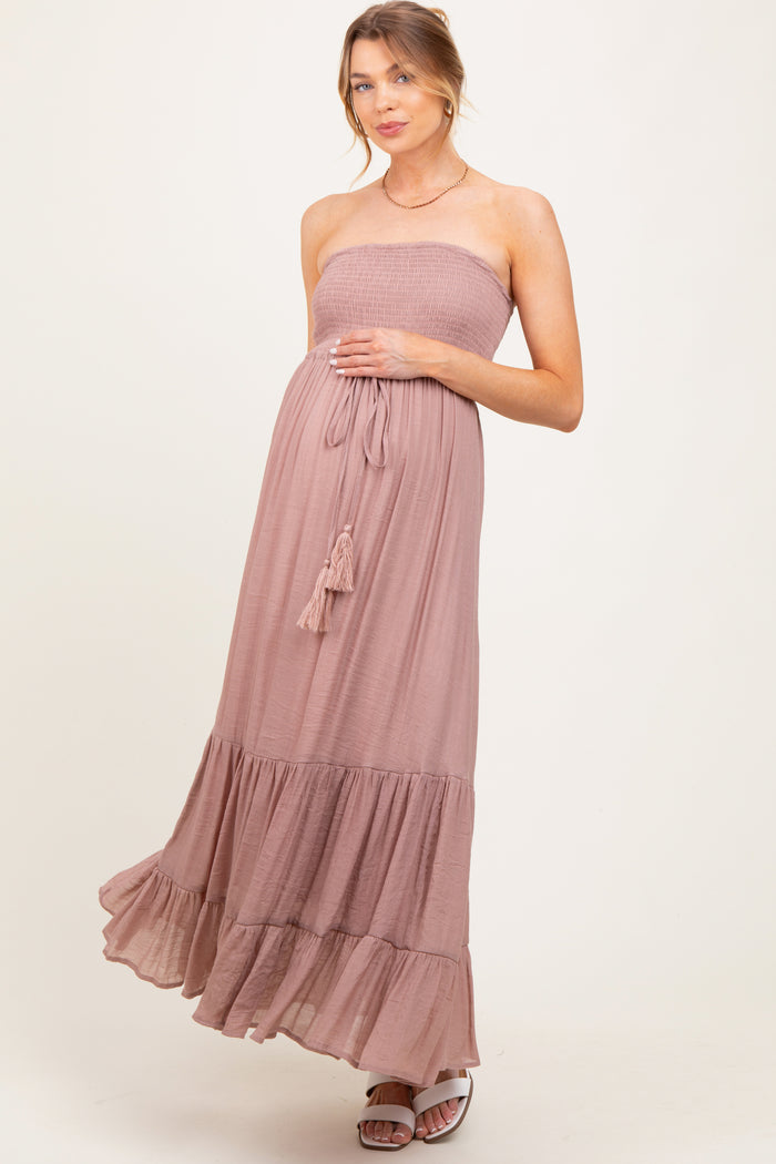 woman wearing a dusty rose strapless maternity dress with smocking and ruffle hem, gently cradling her baby bump