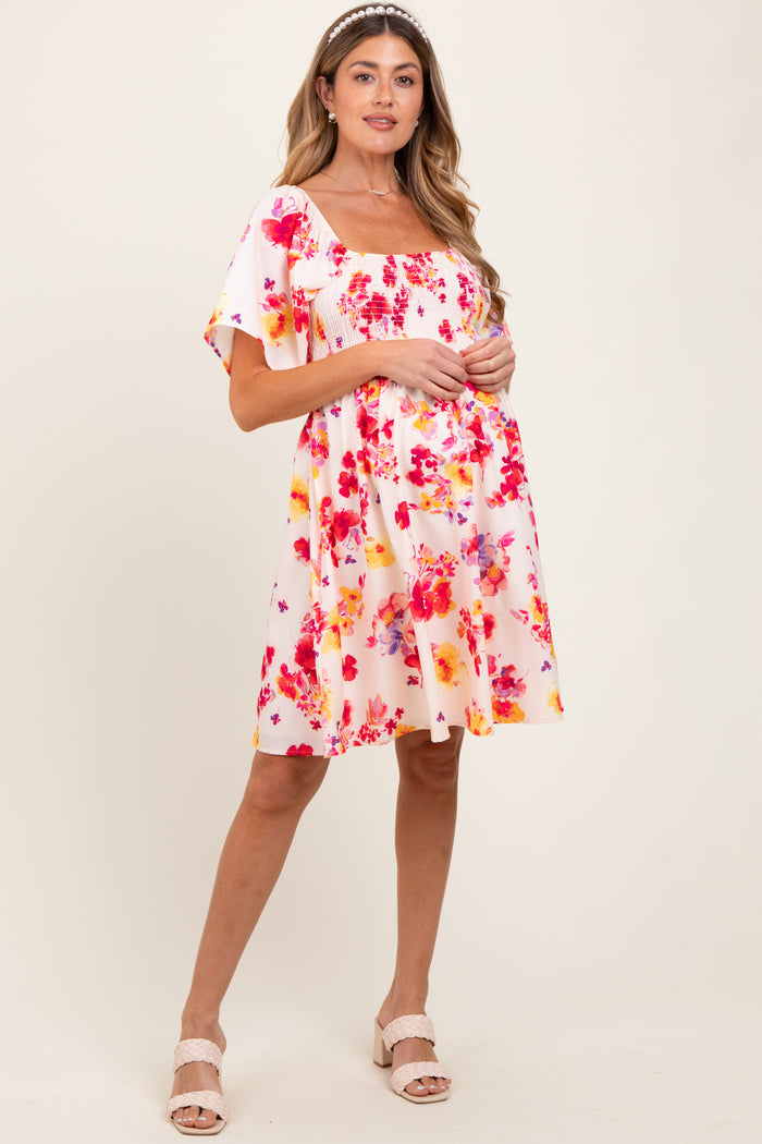 woman wearing a floral print short sleeve maternity dress with a square neckline and pink and orange hues, holding her baby bump