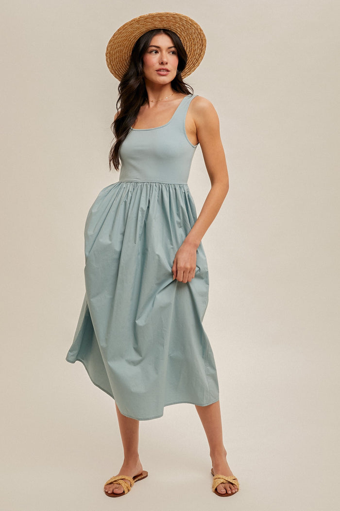 woman wearing a light blue sleeveless midi dress with a gathered waist and a natural straw hat