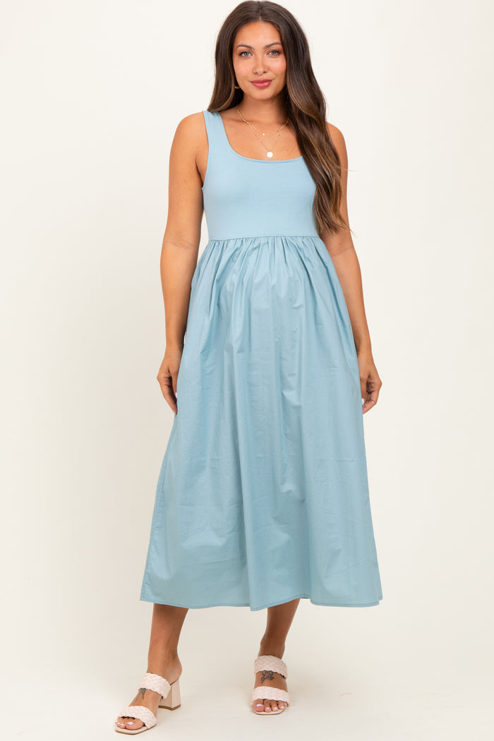 woman wearing a light blue maternity dress with a fitted bodice and flowy skirt, standing against a neutral background