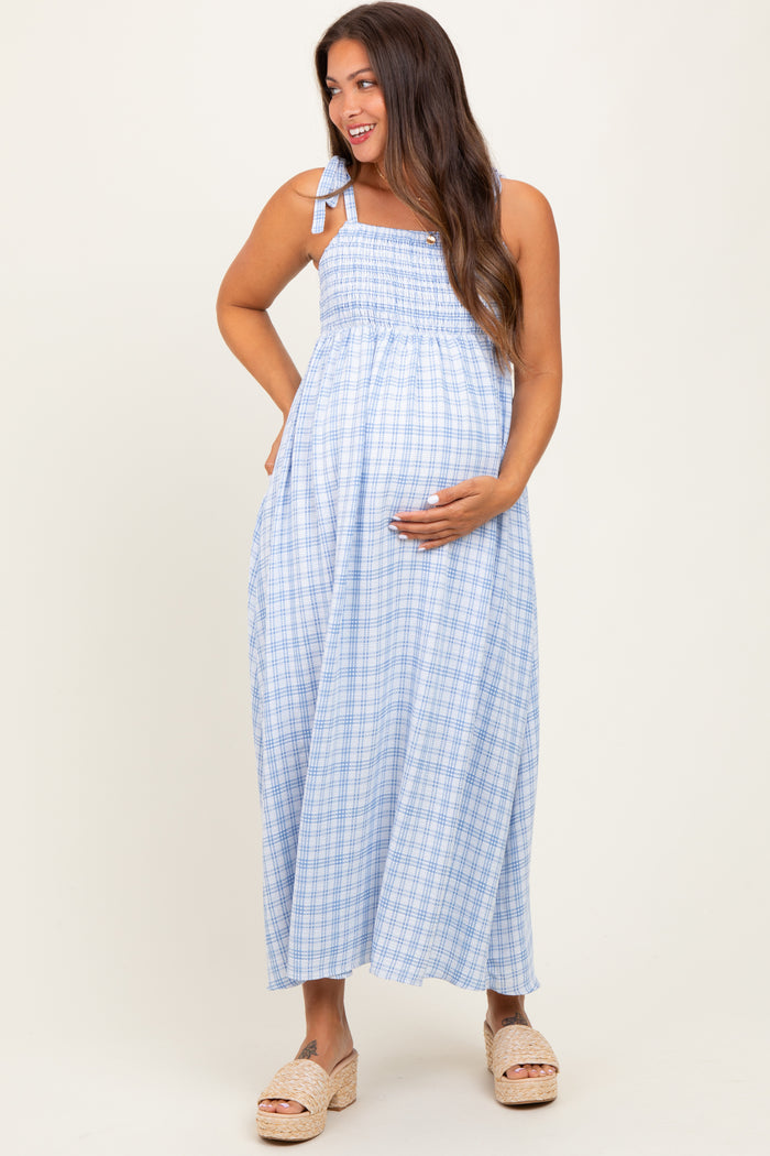 woman wearing a light blue gingham maternity maxi dress with adjustable straps and holding her baby bump