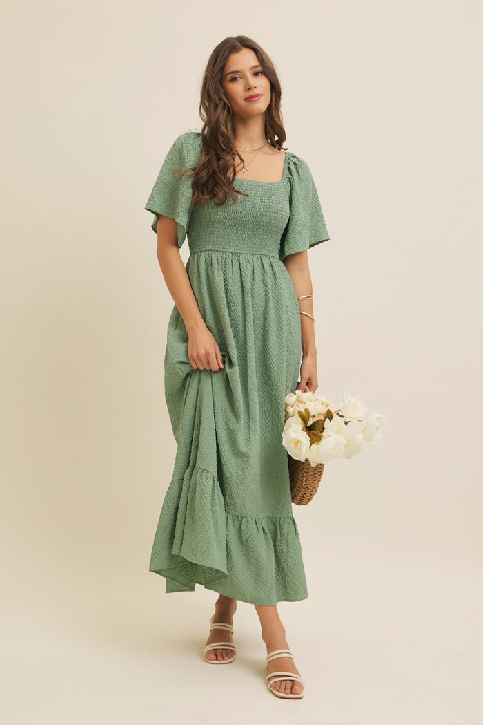 woman wearing a green puff sleeve maxi dress with a smocked bodice and ruffle hem, holding a bouquet of flowers