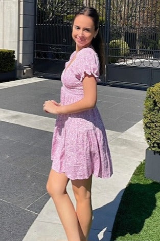 woman wearing a pink floral short sleeve dress, smiling while standing outdoors