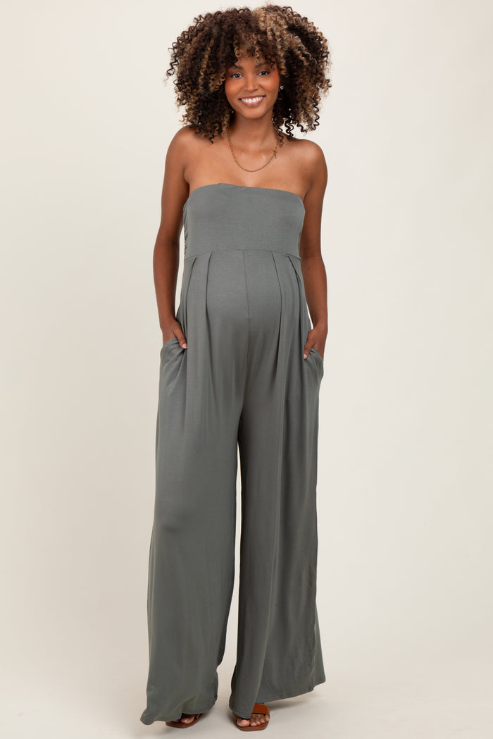 woman wearing a green strapless maternity jumpsuit with wide legs and pockets, showing her baby bump