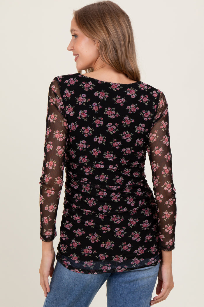 woman wearing a black long sleeve top with floral print and sheer sleeves, showing a ruched back detail
