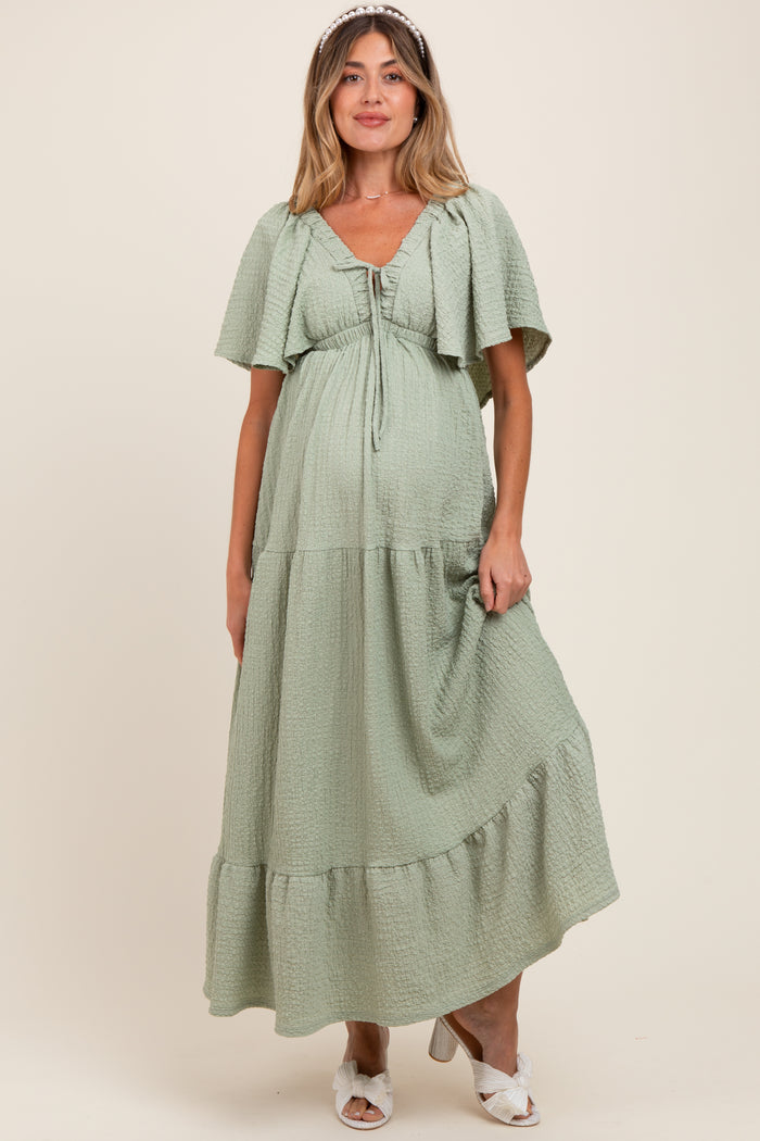 woman wearing a light green maternity maxi dress with flutter sleeves and a tiered hem, showing her baby bump