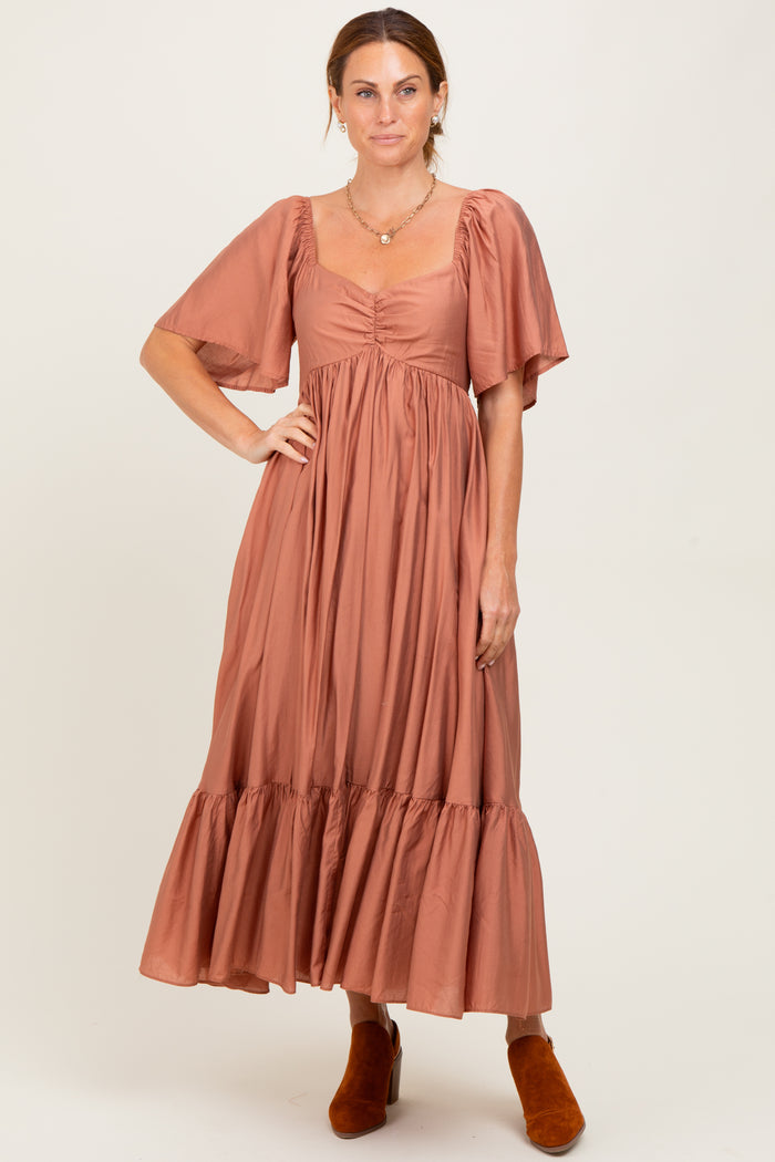 woman wearing a rust colored midi dress with puff sleeves and a tiered skirt, paired with orange ankle boots