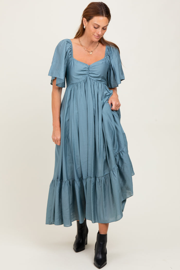 woman wearing a teal puff sleeve midi dress with a square neckline and ruffled hemline, paired with black ankle boots