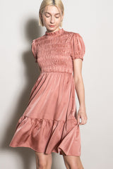 woman wearing a blush pink short sleeve smocked dress with a tiered skirt and ruffled hem